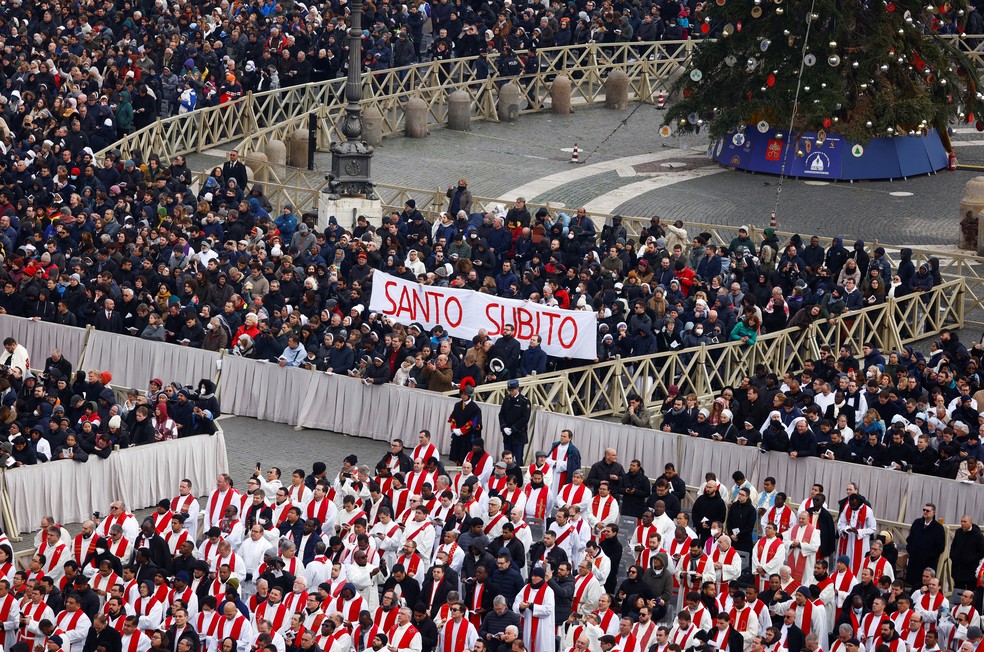Fieis exibem cartaz com os dizeres 'santo subito' (santo agora, em italiano) durante funeral do papa emérito Bento XVI, em 5 de janeiro de 2023.  — Foto: Guglielmo Mangiapane/ Reuters