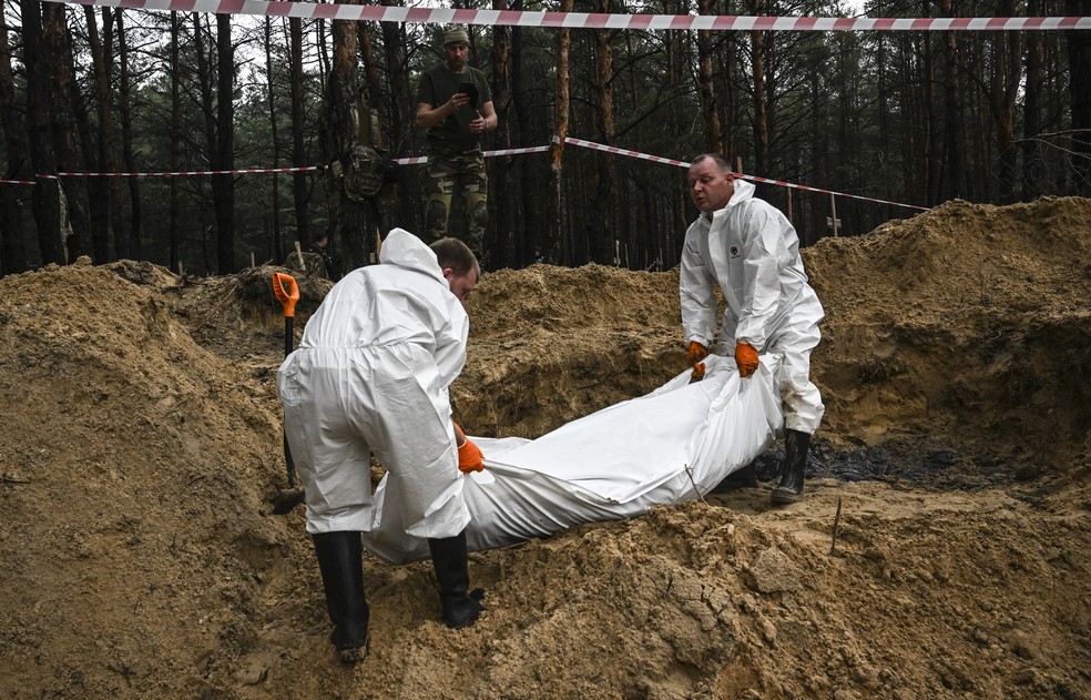 Técnicos forenses retiram corpo de vala comum na cidade ucraniana de Izium — Foto: Juan BARRETO / AFP