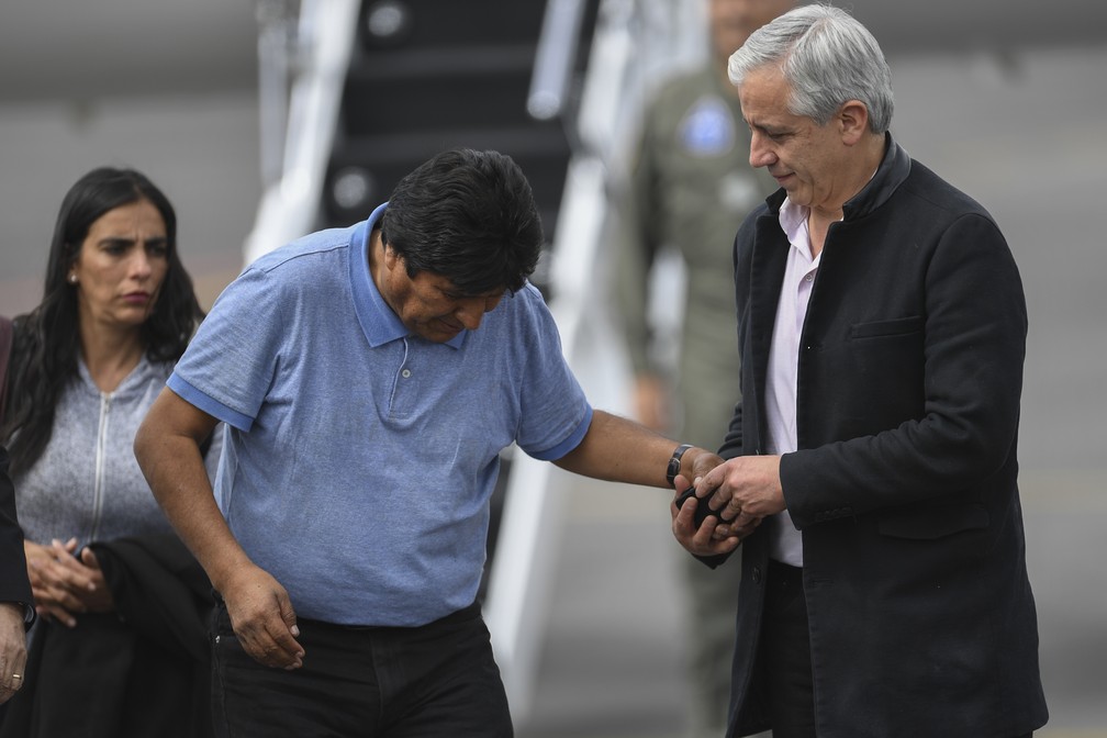 Evo Morales é ajudado pelo ex-vice-presidente Alvaro García Linera ao preparar-se para amarrar o sapato ao chegar na Cidade do México — Foto: AFP/Pedro Pardo