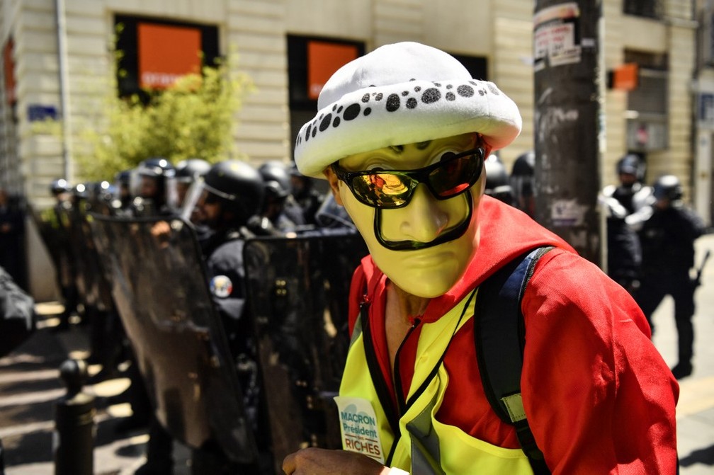 Um homem usando uma máscara do "Anônimo" e um colete amarelo passa pela tropa de choque durante os protestos de 1º de maio, nesta quarta-feira, pelo Dia do Trabalho, em Marselha, na França. — Foto: Christophe Simon / AFP