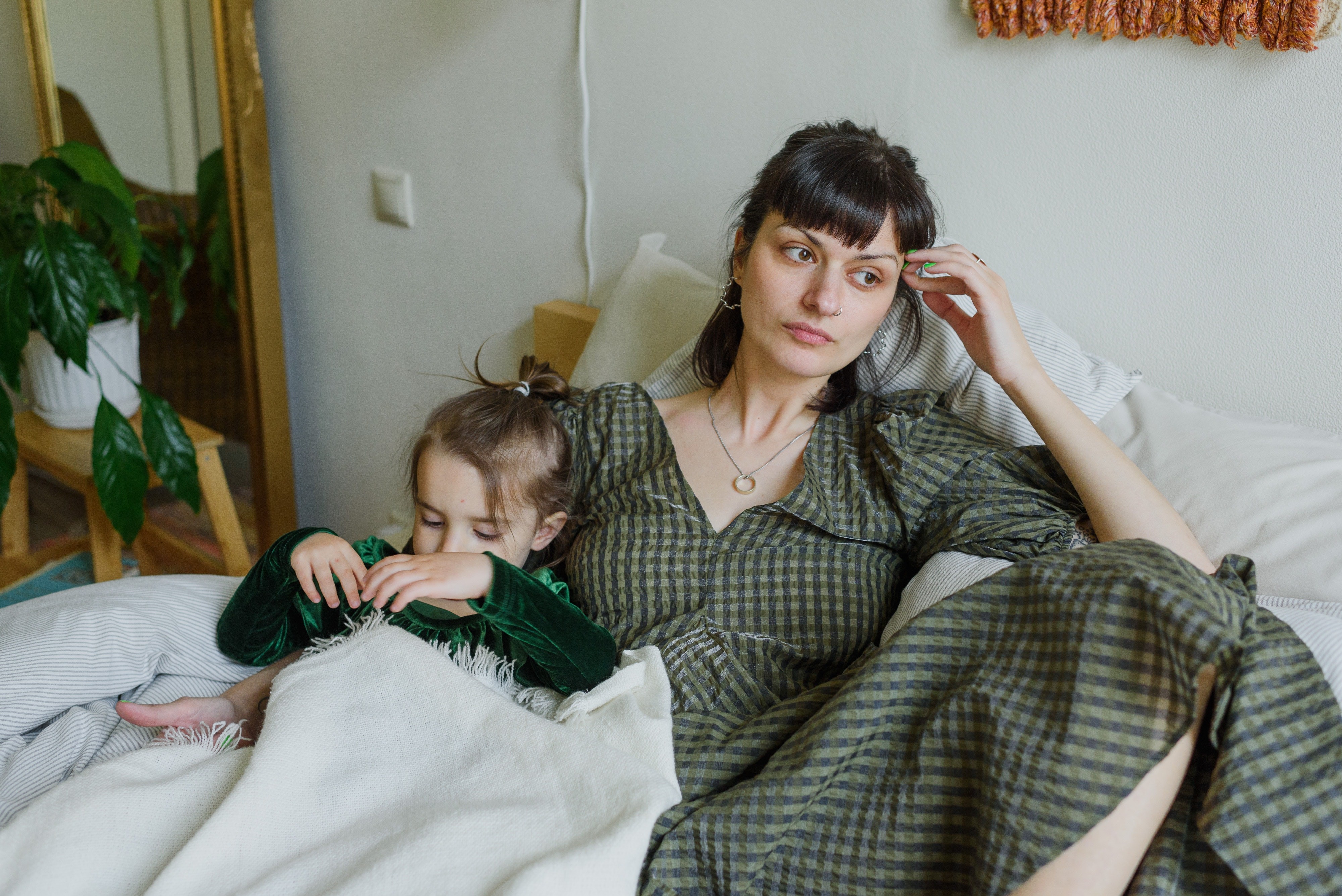 Mãe cansada olhando para o lado com filha deitada (Foto: Ksenia Chernaya/ Pexels)