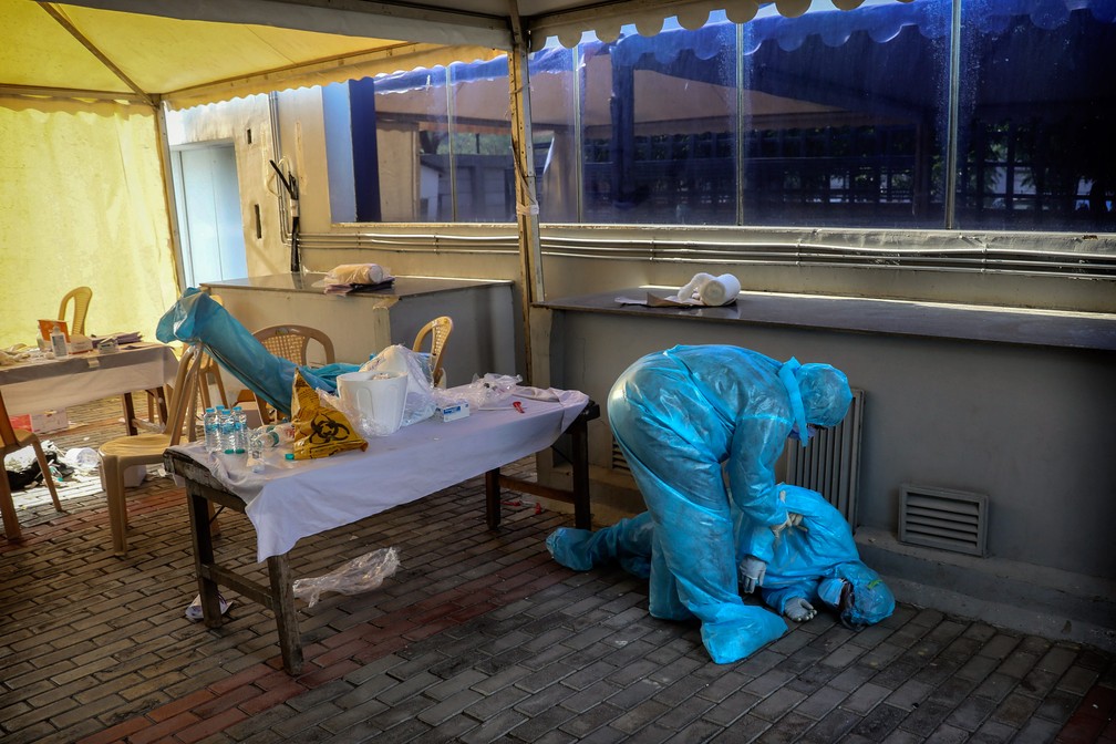 27 de abril - Um membro de uma equipe médica atende sua colega que desmaiou por exaustão em um campo de testes de Covid-19 em Nova Delhi, na Índia  — Foto: Manish Swarup/AP