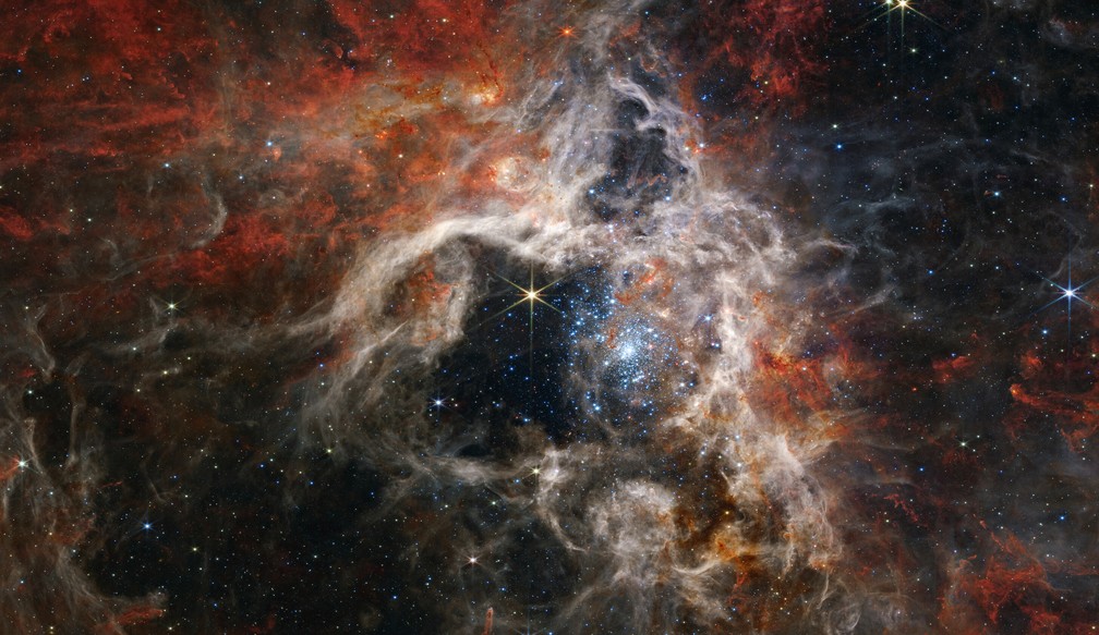 A Nebulosa da Tarântula, uma região de formação de estrelas a 161.000 anos-luz de distância da Terra. No centro, em azul-claro, um aglomerado de estrelas é visível. — Foto: NASA, ESA, CSA, and STScI/Divulgação