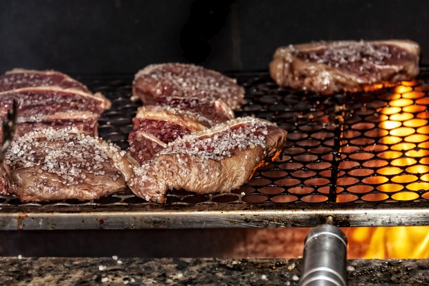 At the barbecue grill , several pieces of beef seasoned with coarse salt are being grilled. You can see the fire under the grill on the right.This cut of meat in Brazil is known as picanha,In Brazil, homemade barbecue is served in all kinds of celebrati (Foto: Getty Images)