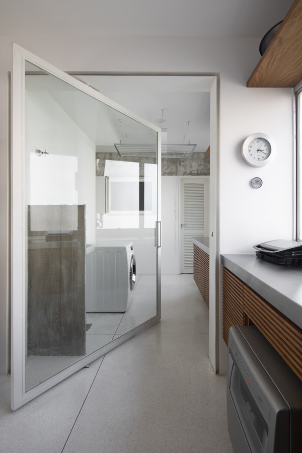 A porta de vidro com moldura de ferro pintada de branco divide a lavandaria e a cozinha