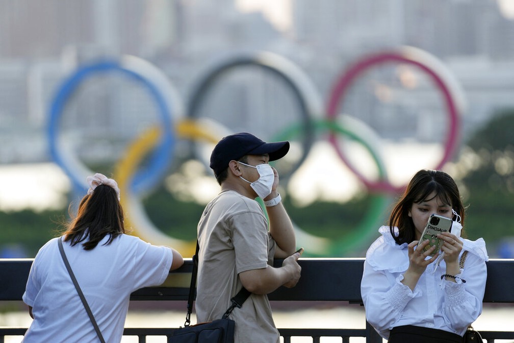 Pessoas passam em frente aos anéis olímpicos em Tóquio, no Japão, no domingo (25) — Foto: Eugene Hoshiko/AP Photo