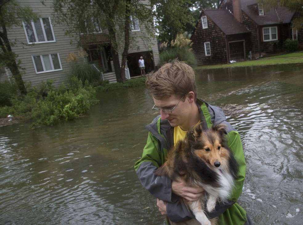 Homem carrega cachorro para atravessar ruas inundadas na cidade de Norfolk, na Virgínia, nos EUA — Foto: Kaitlin McKeown/The Virginian-Pilot via AP
