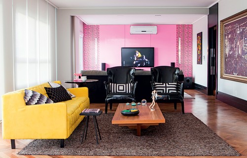 Assinado pela arquiteta Andrea Murao, o projeto tem ambientes amplos, como este espaço que funciona como sala de TV e de estar. Destaque para a parede rosa da televisão, com detalhes decorativos nos cantos