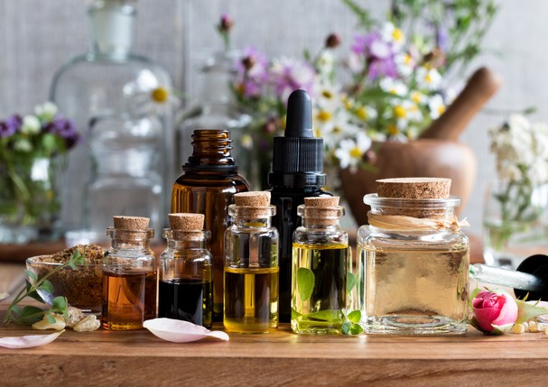 Selection of essential oils, with herbs and flowers in the background (Foto: Getty Images/iStockphoto)