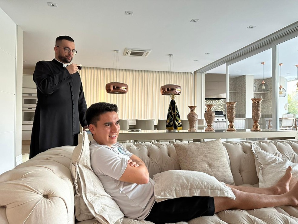 Atuesta ao lado do padre Rodrigo Rodrigues em casa, com imagem de Nossa Senhora Aparecida ao fundo  — Foto: Emilio Botta