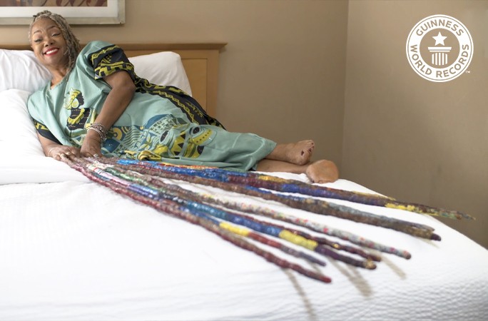 Imagem de Diana Armstrong deitada em sua cama com suas unhas de 13 metros (Foto: Reprodução do site oficial da Guinness World Records)
