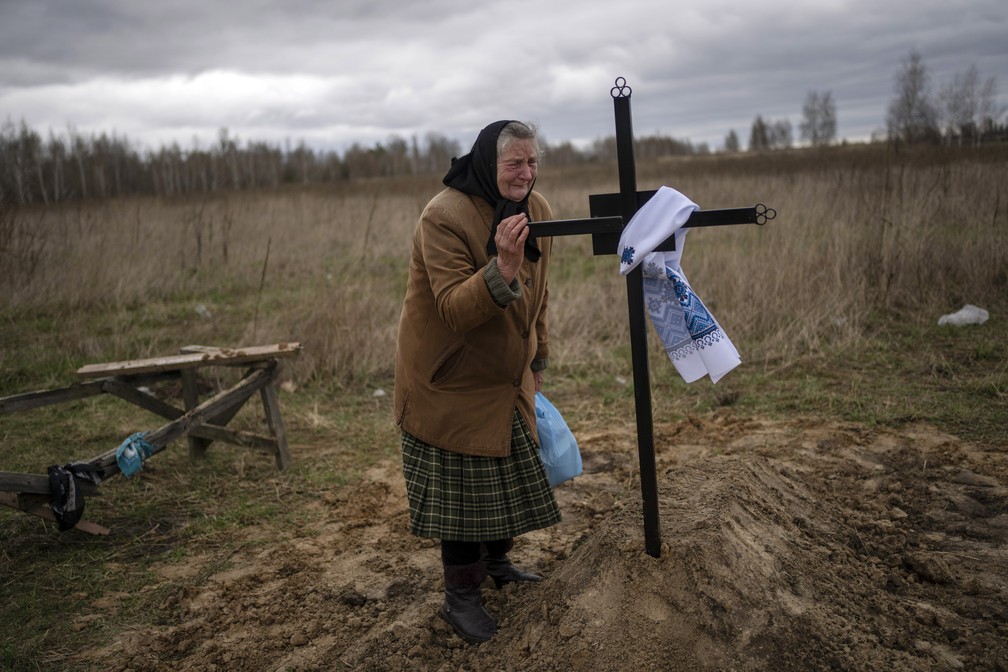 Nadiya Trubchaninova, 70, chora enquanto segura a cruz sobre o túmulo de seu filho Vadym, 48, morto por soldados russos em 30 de março de 2022 em Bucha, na Ucrânia. — Foto: Rodrigo Abd/AP
