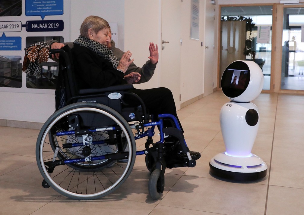 A belga Andree Desmaelle, de 76 anos, se comunica com alguém por chamada com vídeo graças a um robô em um abrigo de idosos de Ostend, na Bélgica, na segunda-feira (16). A empresa ZoraBots disponibilizou alguns robôs para casas de repouso, para ajudar os idosos a manterem contato com família e amigos durante período em que as visitas a esses lugares foram limitadas — Foto: Yves Herman/Reuters