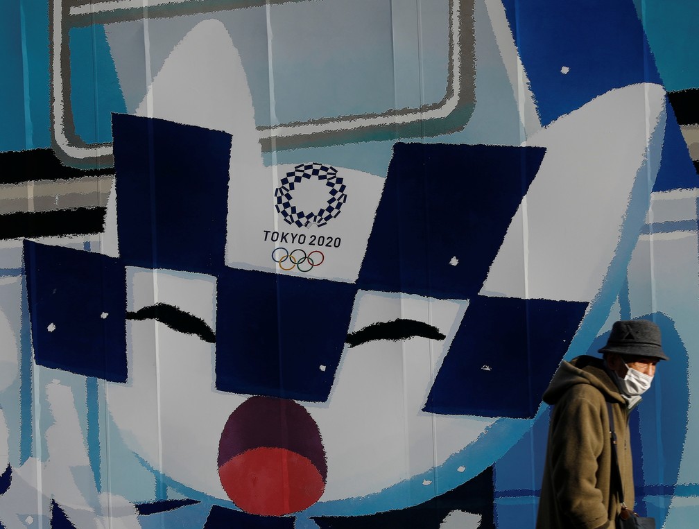 Homem usa máscara ao caminhar em 3 de fevereiro diante de painel em Tóquio, no Japão, com Miraitowa, o mascote dos Jogos Olímpicos transferidos para 2021 — Foto: Kim Kyung-Hoon/Reuters