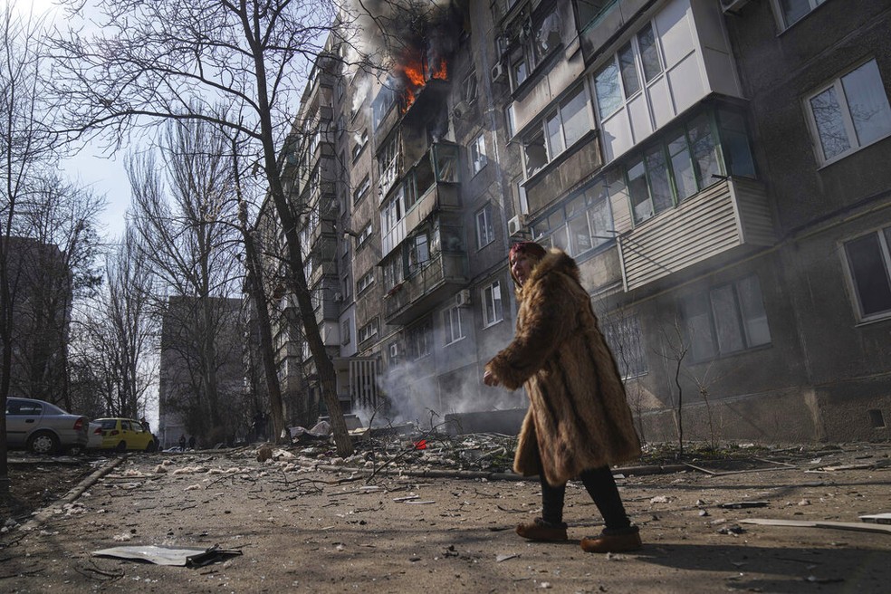 Mulher caminha diante de prédio atingido por bombardeio russo em Mariupol, no sul da Ucrânia, em março de 2022. — Foto: Evgeniy Maloletka/ AP