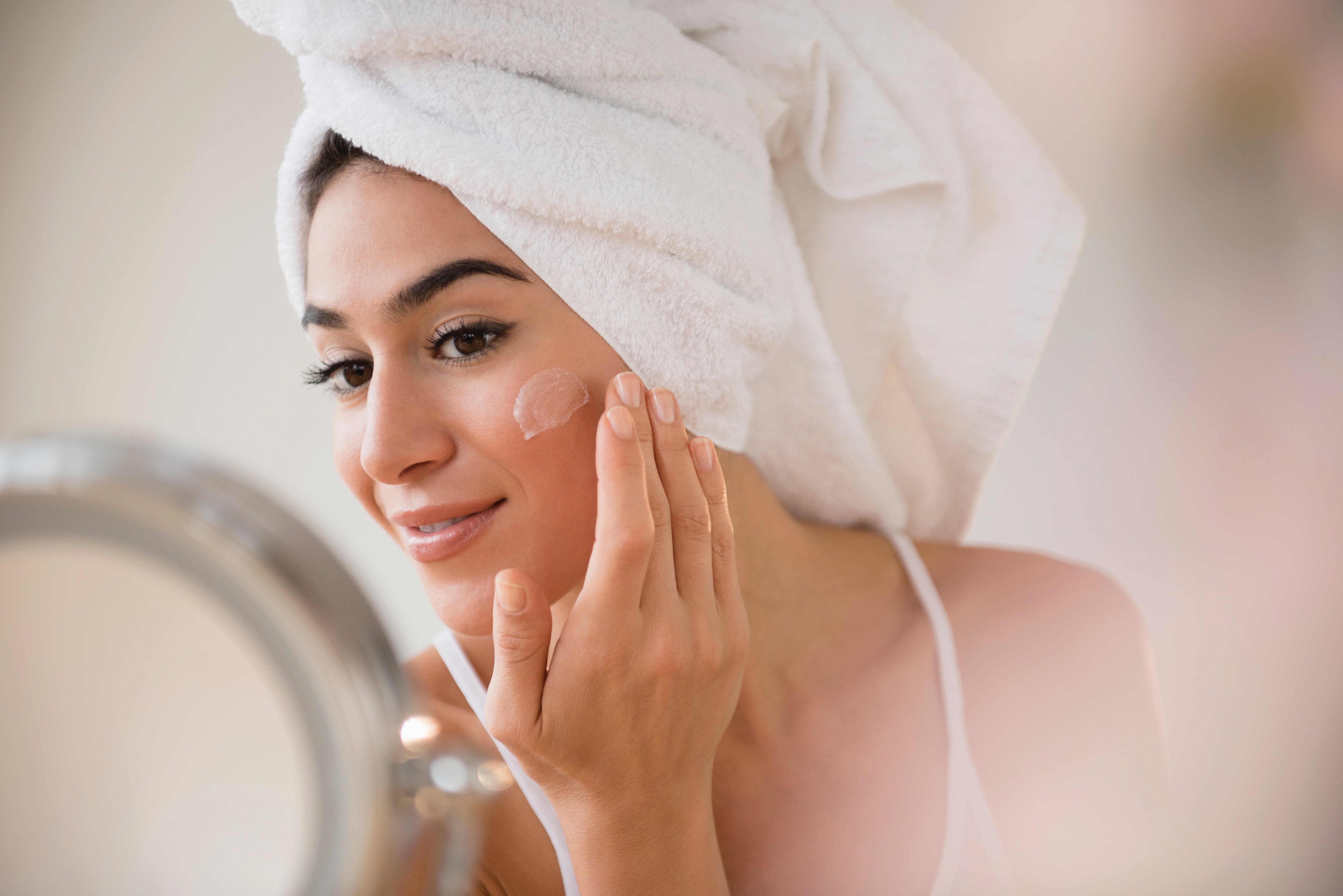 Woman with hair in towel rubbing lotion on face (Foto: Getty Images/Tetra images RF)