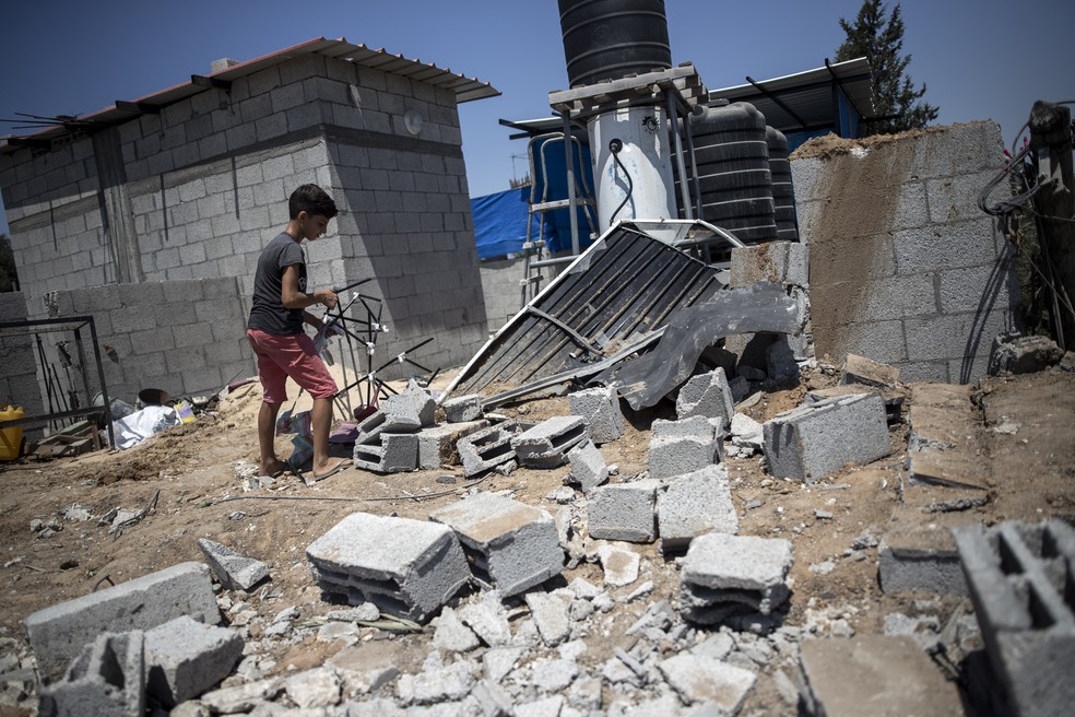 Um menino palestino verifica os danos à casa de sua família após ataques aéreos no campo de refugiados de Buriej, na Faixa de Gaza, no sábado (15) — Foto: Khalil Hamra/AP