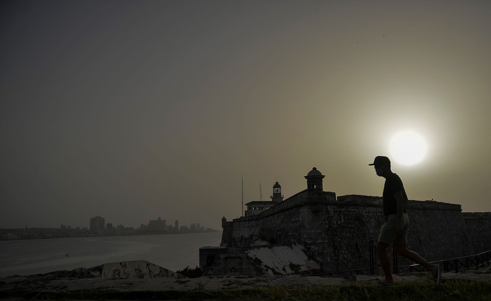 Homem caminha perto do Castelo de Morro enquanto nuvem de poeira do Saara encobre a cidade de Havana, em Cuba, na quarta-feira (24)  — Foto: Yamil Lage / AFP
