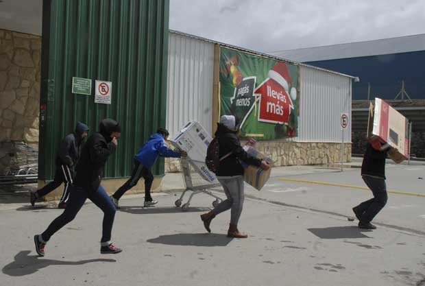 Pessoas correm com itens roubados de supermercado em Bariloche, Argentina, nesta quinta-feira (20) (Foto: AP)