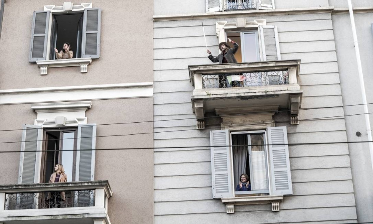 Vizinhos interagem das sacadas de seus apartamentos em Milão, Itália, em março de 2020. Novas formas de socializar em tempos de pandemia — Foto: ALESSANDRO GRASSANI / The New York Times