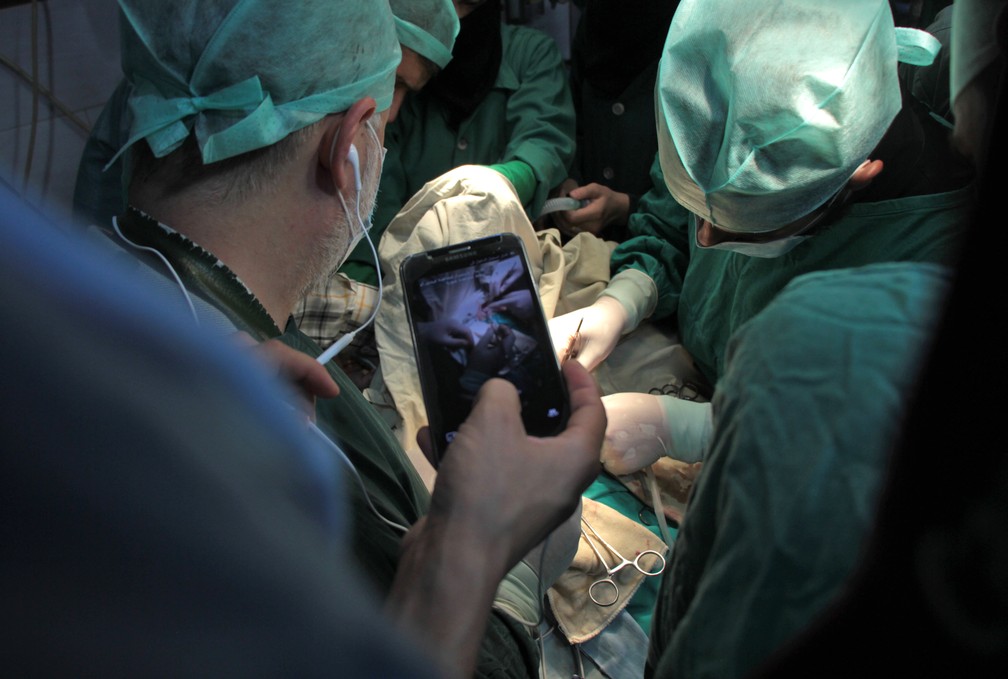 Cirurgião segura telefone para transmitir cirurgia em tempo real a partir de hospital em Duma, na Síria (Foto: Hamza Al-Ajweh)
