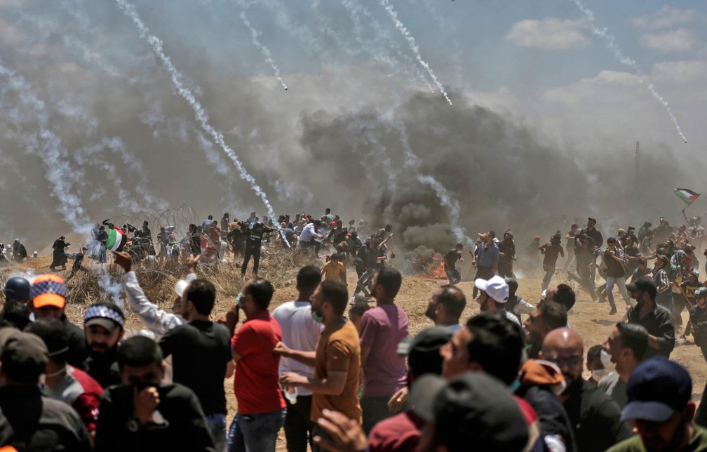 Palestinos correm para se proteger de bombas de gás atiradas por tropas israelenses na fronteira entre Gaza e Israel após protestos contra a inauguração da embaixada dos EUA em Jerusalém (Foto: Mahmud Hams/AFP)