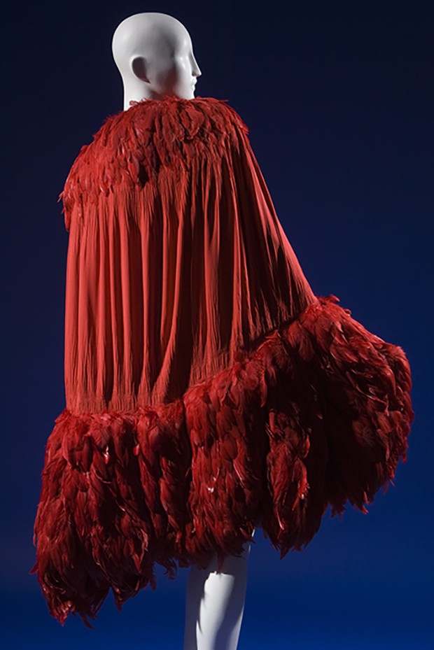 Calf length evening cape in doubled scarlet silk crepe de chine crinkled and "smocked" along curved  edges of cocoon silhouette, crimson feather trim forming "shawl collar" and wide hem band (Foto: Divulgação/ Cortesia do Museum at FIT)