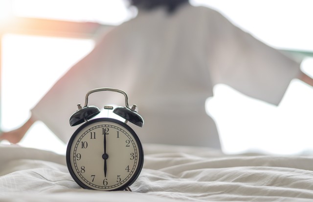 Woman on bed wake up stretching in bedroom with alarm clock at 6.00 a.m. morning. Biological Clock healthcare concept. (Foto: Getty Images/iStockphoto)