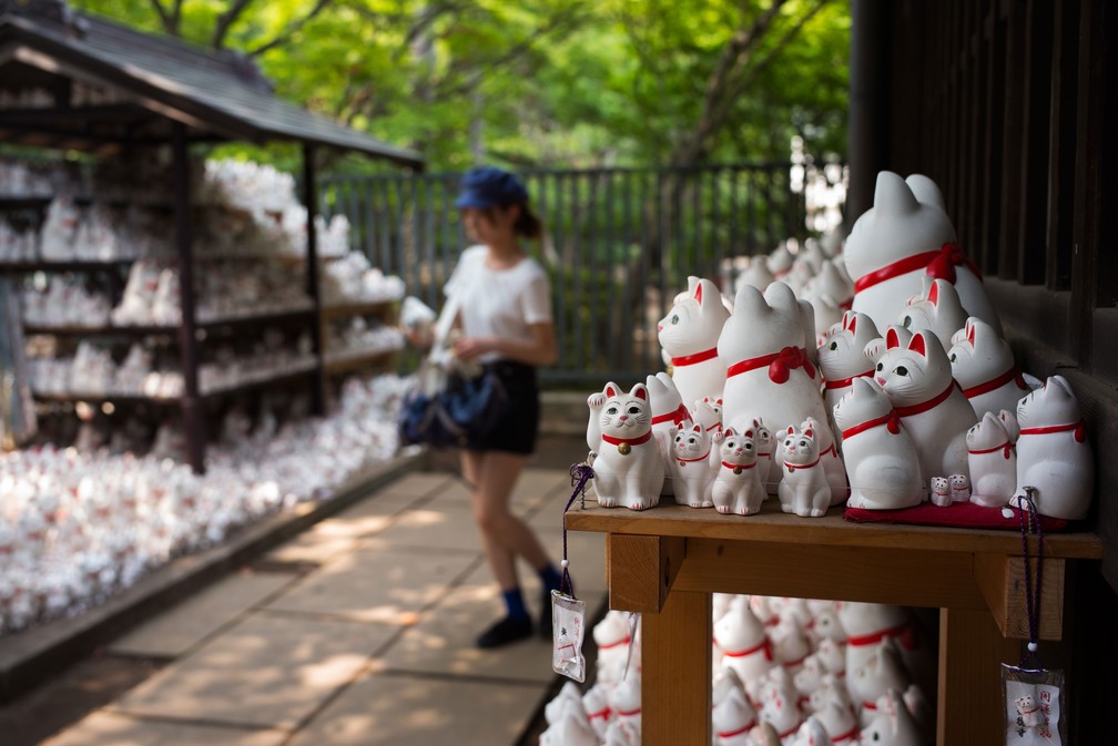 Mulher caminha entre gatos ‘maneki-neko’ no templo Gotokuji, em Tóquio — Foto: Martin Bureau / AFP