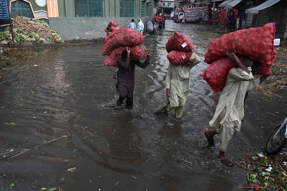 Trabalhadores tentam salvar alimentos em um mercado inundado, em Lahore — Foto: Arif ALI/AFP