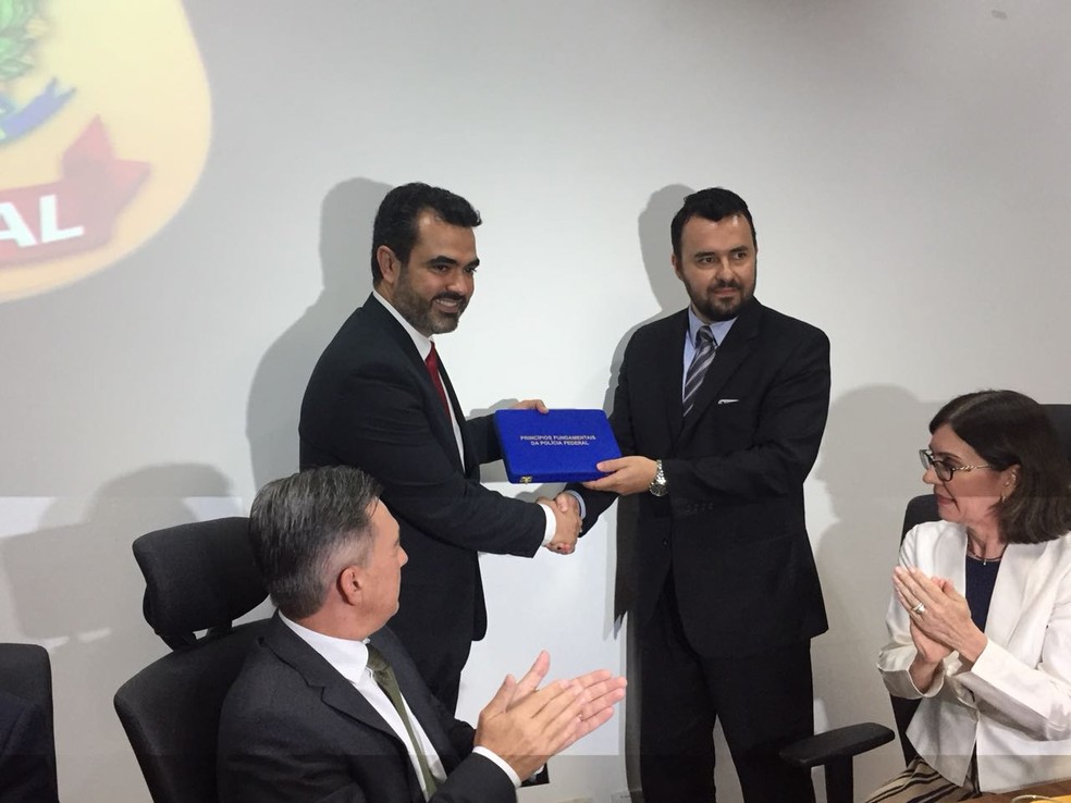 Acompanhado do secret&aacute;rio de Justi&ccedil;a e Seguran&ccedil;a P&uacute;lica de MS e da diretora executiva da PF, Lima, &agrave; esquerda, recebe do ex-superintendente o emblema com princ&iacute;pios fundamentais da PF (Foto: Dyego Queiroz/G1 MS)