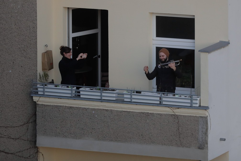 Um homem ri depois de tocar a Sinfonia n.º 9, de Beethoven, em uma varanda no distrito Prenzlauer Berg em Berlim, na Alemanha, no domingo (22). Para retardar a propagação do coronavírus, o governo alemão restringiu consideravelmente a vida pública e pediu aos cidadãos para ficarem em casa — Foto:  Markus Schreiber/AP
