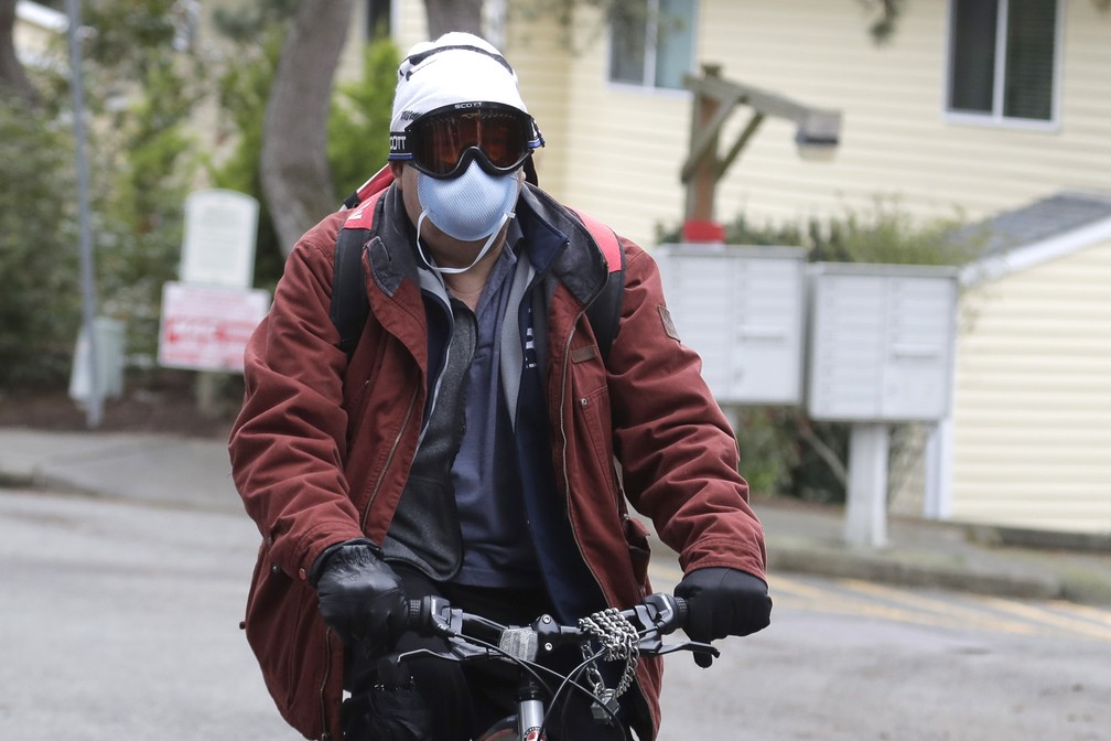 Homem usando máscaras e óculos anda de bicicleta em Kirland, Washington, perto de Seattle, na terça-feira (3). A OMS recomenda o uso de máscaras apenas para profissionais de saúde e pessoas que estão doentes. — Foto: Ted S. Warren/AP