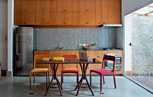A cozinha projetada pelo arquiteto Gustavo Calazans tem ilha central e mesa de jantar. De madeira rústica, ela é acompanhada de cadeiras de design amarelas