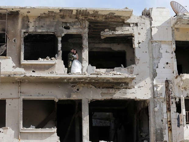 Casal posa para foto em prédio da cidade de Homs devastada pela guerra na Síria (Foto: AFP PHOTO/JOSEPH EID)