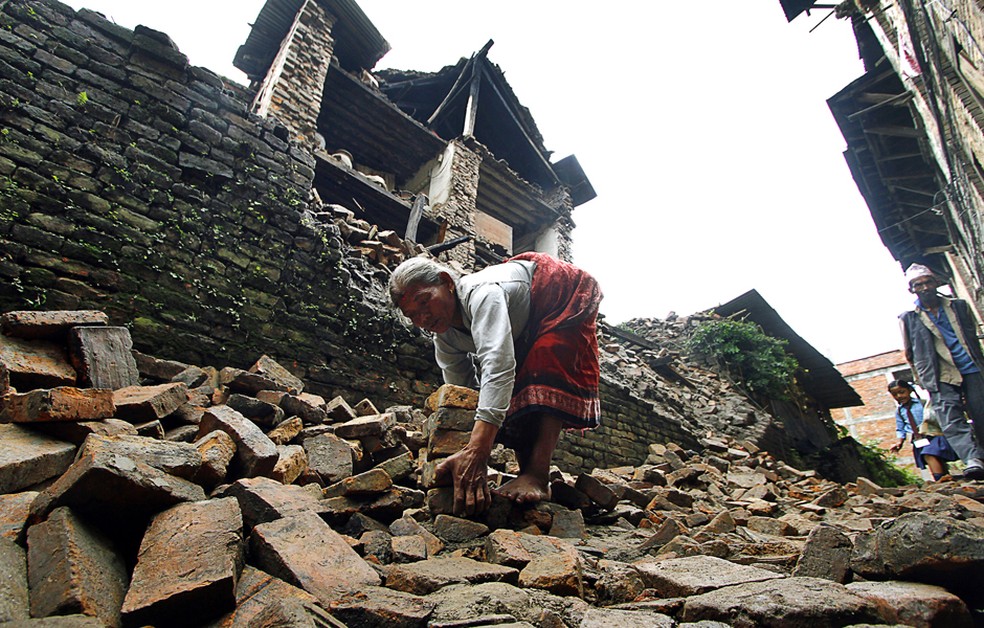 Em imagem de 2016, mulher recolhe pedras após terremoto no Nepal. — Foto: Niranjan Shrestha/ AP Photo