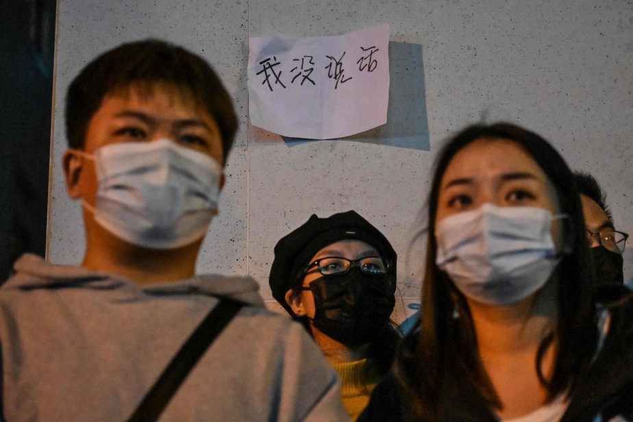 De máscaras, manifestantes protestam em Xangai; no fundo, cartaz mostra a frase: 'eu não disse nada'