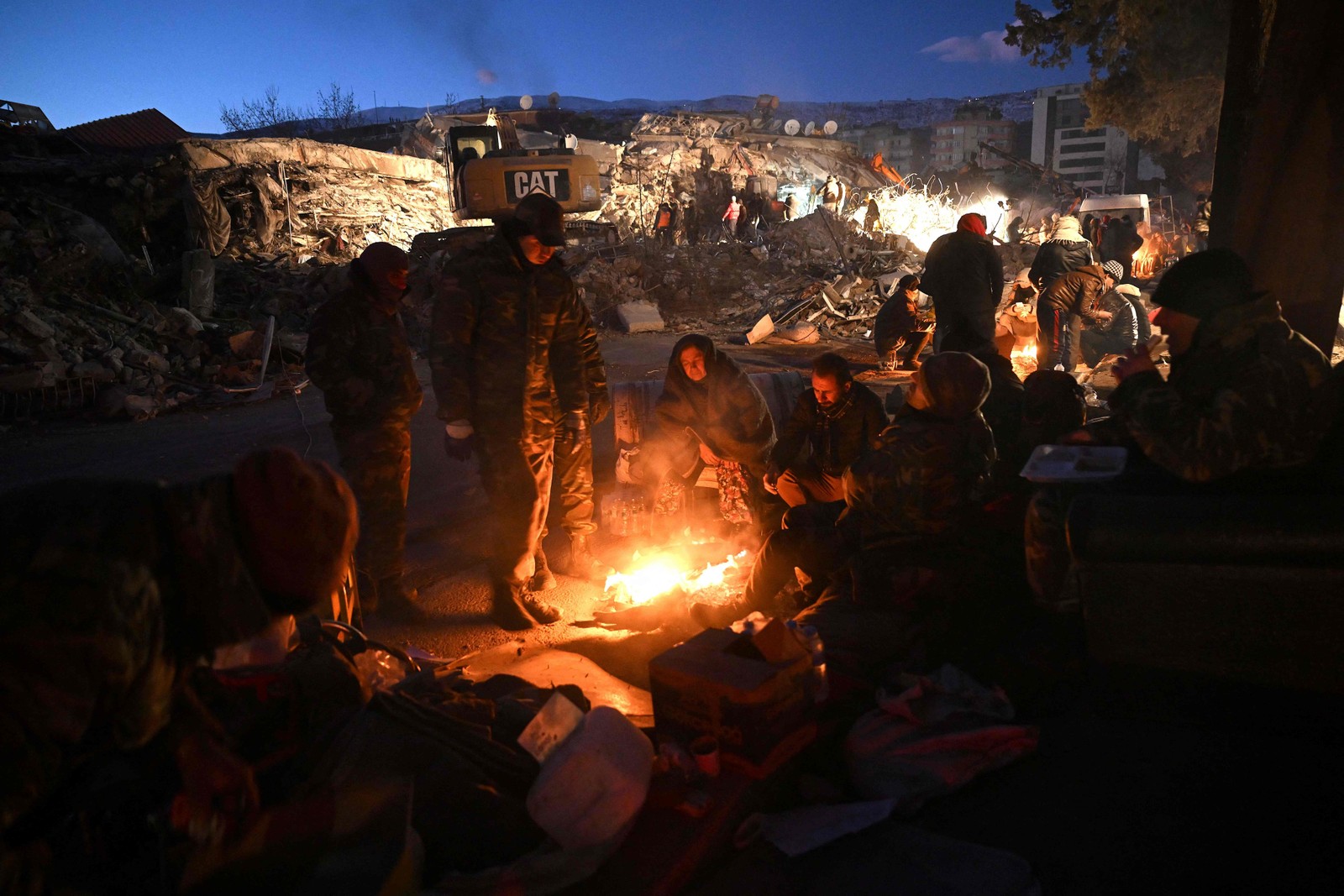 Equipe de resgate do Azerbaijão descansa perto de uma fogueira em meio aos escombros de edifícios desabados em Kahramanmaras, na Turquia — Foto: OZAN KOSE/AFP