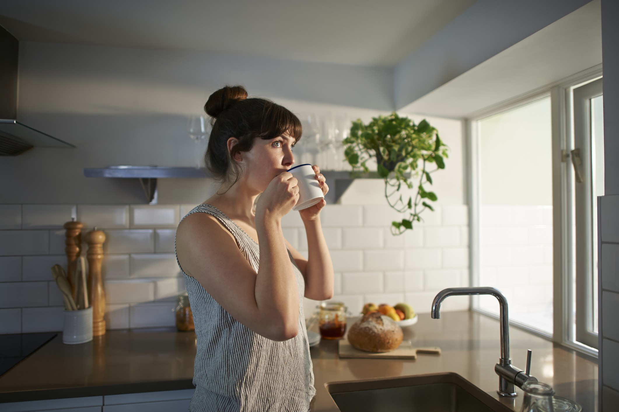A woman standing in her kitchen drinks from a mug. (Foto: Getty Images)