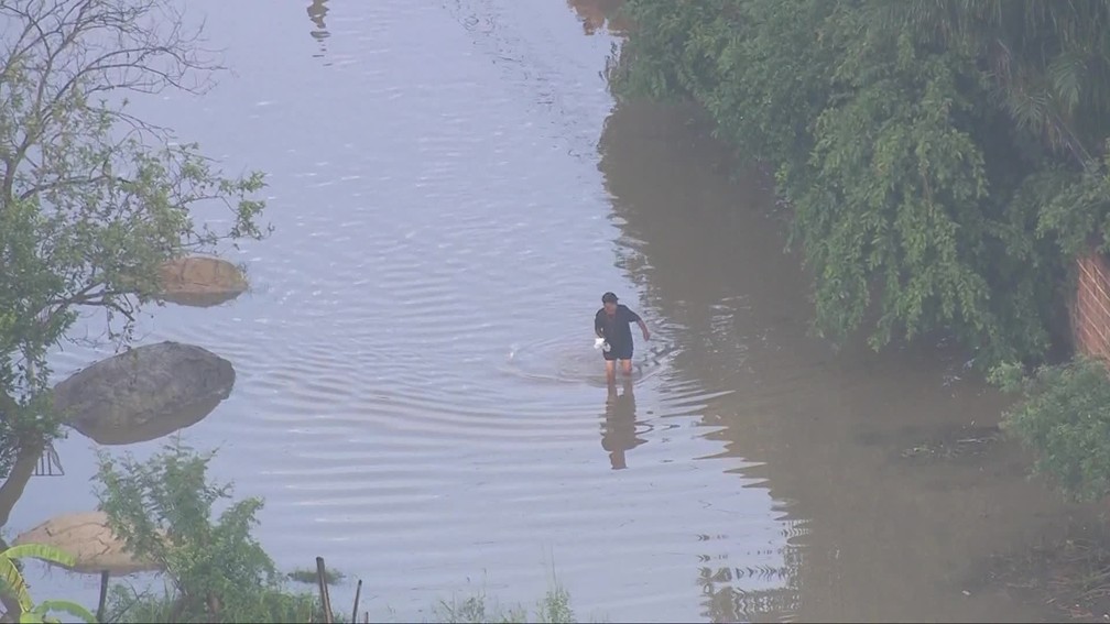 Morador caminha em meio ao alagamento em rua de Seropédica, na Baixada Fluminense — Foto: Reprodução/ TV Globo