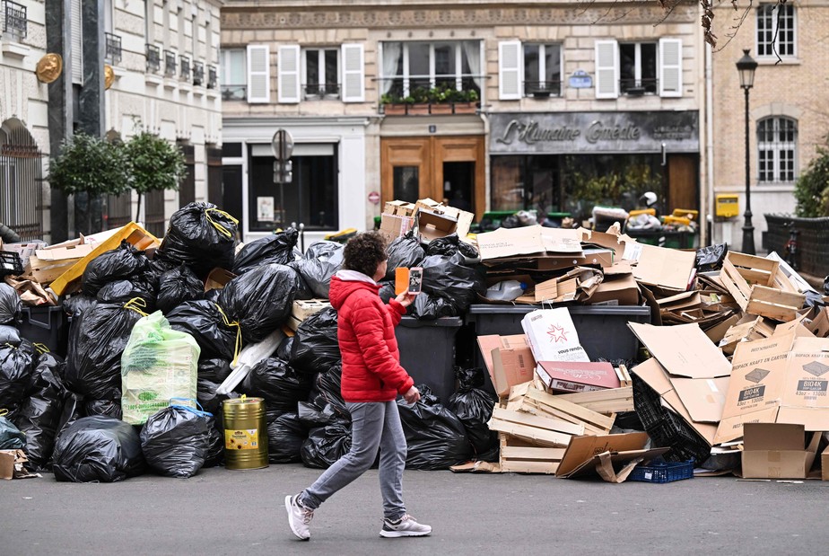 Pedestre passa por um monte de lixo acumulado em uma rua de Paris, durante greve contra a reforma previdenciária proposta pelo governo francês