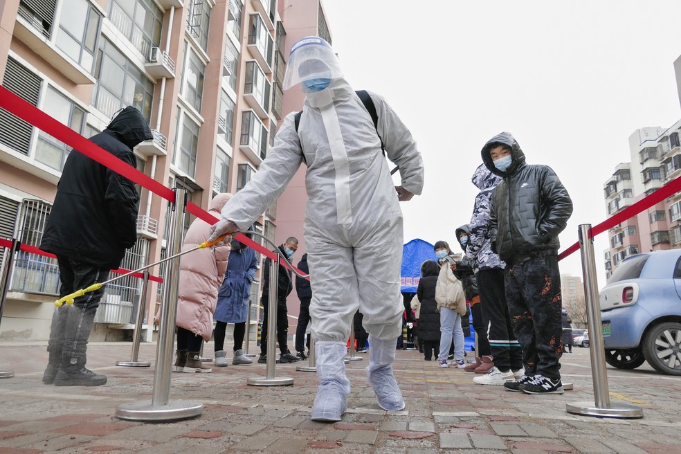 Profissional com roupa de proteção pulveriza desinfetante em uma fila para testes de Covid-19 em massa na cidade de Tianjin, no norte da China, em 9 de janeiro de 2022 — Foto: Chinatopix via AP