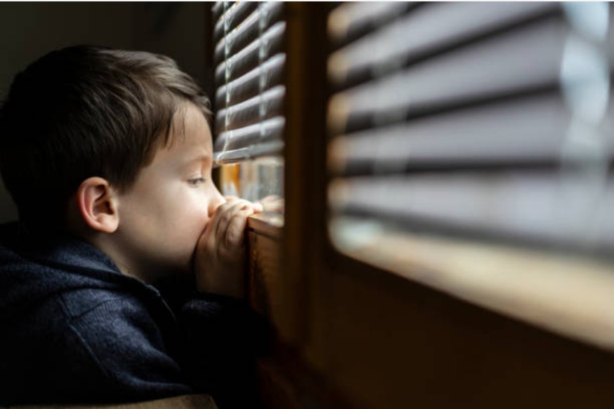 Menino triste dentro de casa olhando pela janela (Foto: Getty Images)