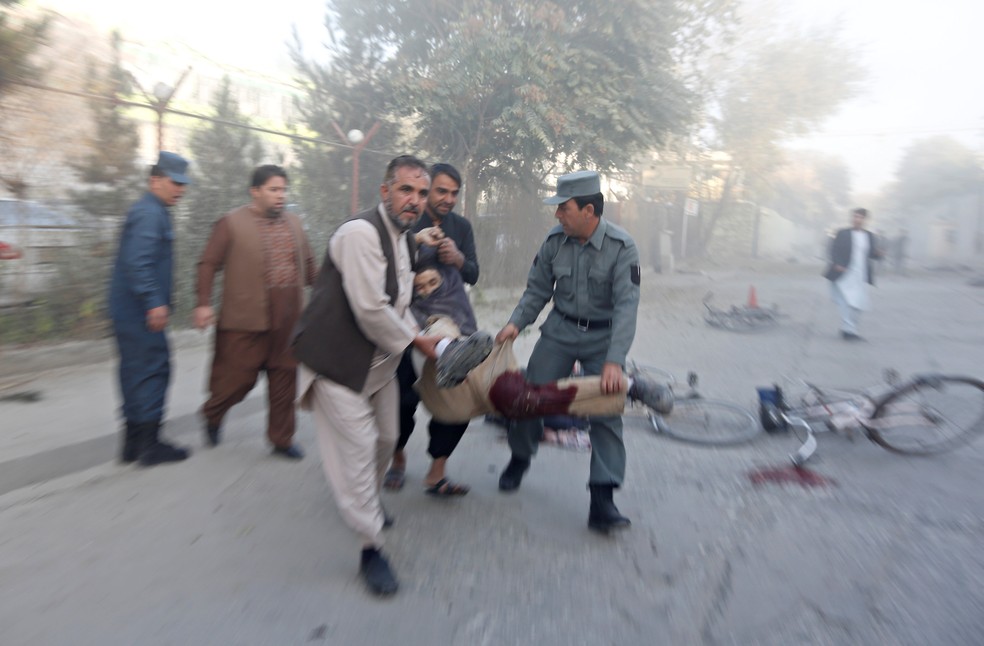 Policiais e civis carregam homem ferido por ataque a canal de TV em Cabul, no Afeganistão (Foto: Reuters/Omar Sobhani)