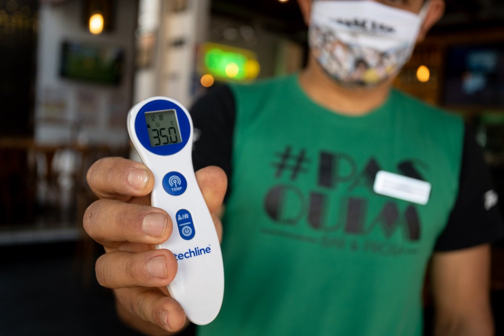 Funcionário de bar na Vila Madalena, em São Paulo, utiliza um termômetro para medir a temperatura dos clientes na entrada do estabelecimento — Foto: Marcelo Brandt/G1
