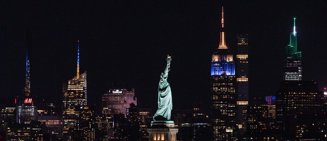 A Estátua da Liberdade é vista ao lado do Empire State Building, iluminada em azul e dourado, em comemoração ao alcance de 70% dos adultos de Nova York que receberam sua primeira dose da vacina Covid-19.