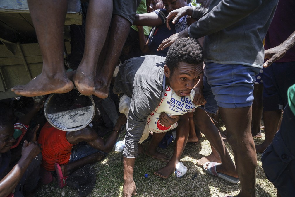 20 de agosto - Homem rasteja após conseguir pegar um saco de arroz de um caminhão de donativos em  Vye Terre, no Haiti — Foto: Fernando Llano/AP
