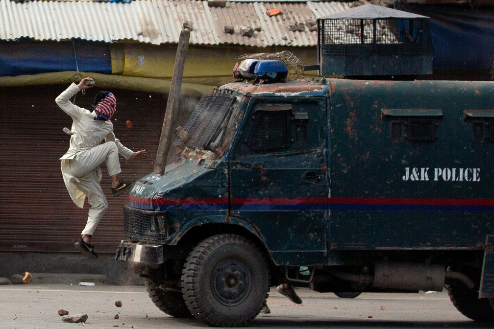 Imagem de maio de 2019 mostra manifestante mascarado de origem caxemira salta atirando pedras contra um veículo blindado da polícia indiana durante protesto em Srinagar, na porção da Caxemira sob controle da Índia — Foto: Dar Yasin/AP