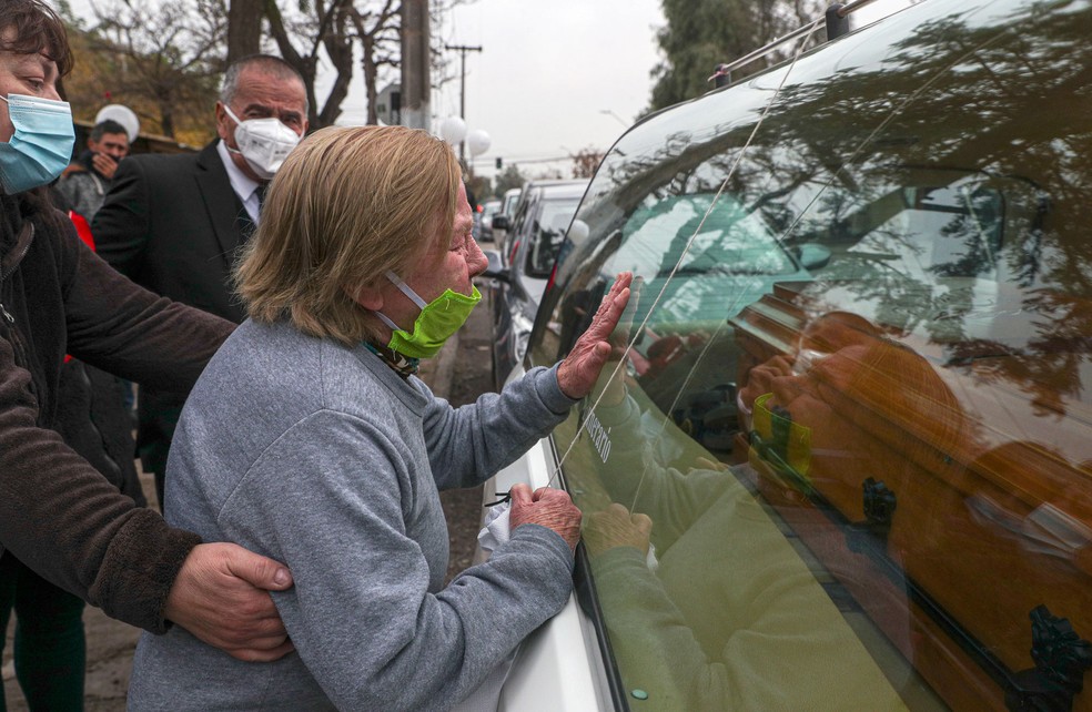 Mulher de 72 anos toca na janela de carro fúnebre que leva corpo de pessoa que teria morrido de complicações de Covid-19, em Santiago, no Chile, na segunda-feira (15)  Foto:  Esteban Felix/AP