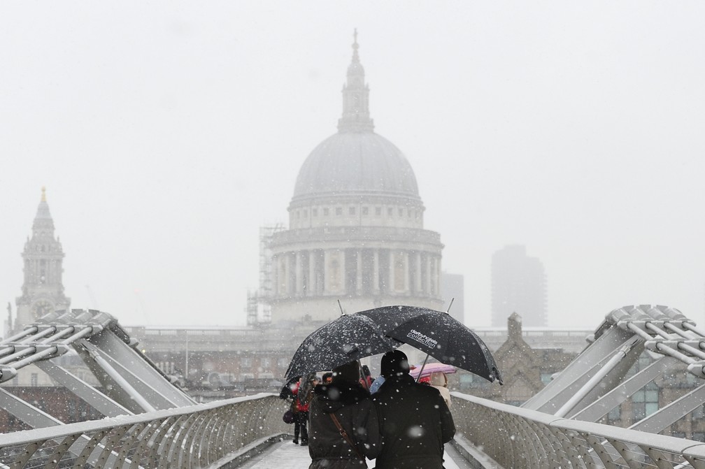 Pedestres se protegem da nevasca em frente à catedral de Saint Paul, em Londres, neste domingo (10) (Foto: Daniel Sorabji/ AFP)